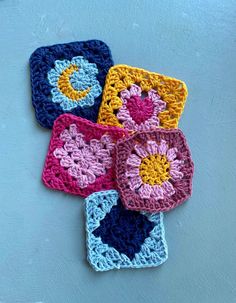 four crocheted squares are arranged on a blue surface, each with a flower in the center