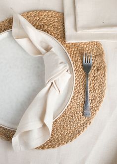 a place setting with napkins, silverware and a straw hat on the table