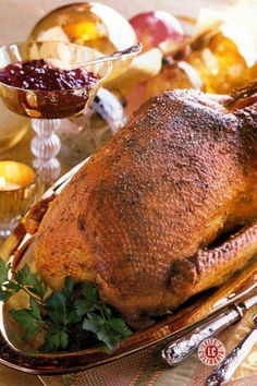 Mahogany-colored whole bird rests on a platter garnished with fresh herbs, sage leaves, and bright cranberries against a dark background.