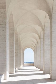 an empty walkway lined with white pillars leading to the ocean