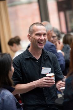 a man is smiling and holding a cup in his hand while standing among other people