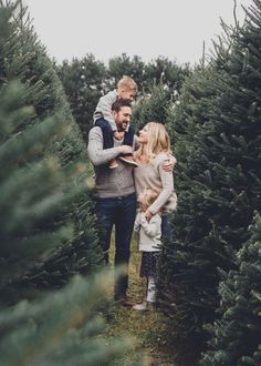 a man and woman are standing in the middle of a christmas tree farm with their two children