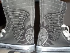 a pair of gray shoes with wings painted on the side and white laces around them