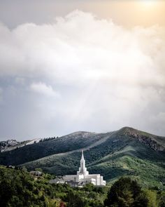 a large white church sitting on top of a lush green hillside under a cloudy sky