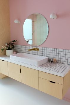 a bathroom with pink walls and white counter tops, mirror on the wall above it