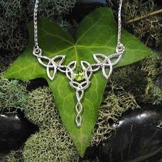 "I've designed this long, statement Celtic inspired necklace entirely in sterling silver featuring a center, faceted 10x8mm peridot gemstone! The frame, or centering, of the pendant is made with Celtic Trinity Knots and sterling wire work braids down the center to add the balancing touches to the piece. It comes with a sterling box chain which is soldered to each end of the pendant. This piece is 18\" in length, including the chain, and the pendant, itself, is approximately 3 inches, in height, May Birthstone Jewelry In Silver With Peridot, Silver Peridot Jewelry For May Birthstone, Silver Peridot Jewelry With Gemstone, Silver Peridot Jewelry For Anniversary, Silver Peridot Birthstone Jewelry, Lime Green Peridot Jewelry For Wedding, Silver Peridot Necklaces For Jewelry Making, Silver Pendant Necklace With Peridot, Sterling Silver Lime Green Gemstone Jewelry