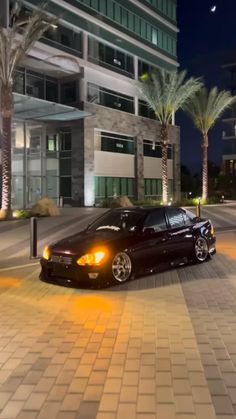 a black car parked in front of a tall building at night with its lights on