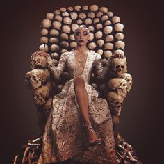 a woman sitting on top of a giant chair with skulls around her head and legs