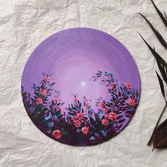 a purple plate sitting on top of a table next to some leaves and flowers in front of it