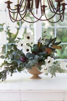 a vase filled with flowers and greenery on top of a table next to a chandelier