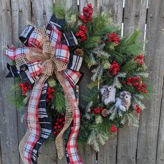 two wreaths on the side of a fence with pine cones, berries and other decorations