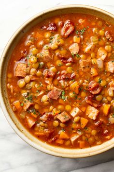 a bowl of soup with ham, beans and carrots on a marble counter top