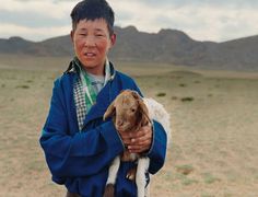 a young boy holding a baby goat in the desert