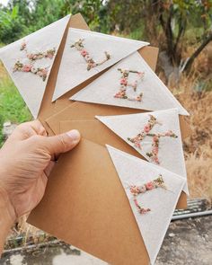 someone is holding up some letters made out of paper with flowers on them in front of trees