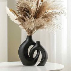 a black vase with some dry grass in it