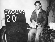 black and white photograph of a man sitting next to a sign