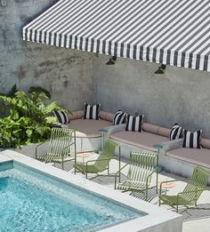 an outdoor pool with lounge chairs next to it and a striped awning on the roof