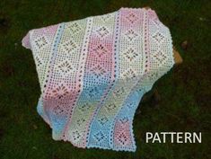 a crocheted blanket sitting on top of a green grass covered in pink and blue yarn