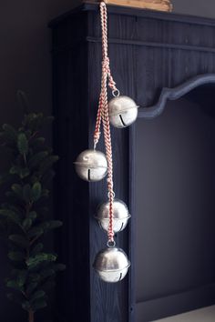 three silver bells hanging from the side of a fireplace mantel next to a christmas tree