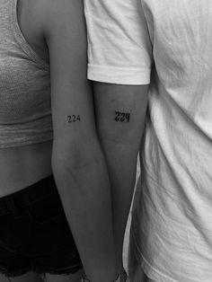 two people standing next to each other with their arms wrapped around one another and numbers tattooed on them