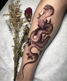 a tattoo on the leg of a woman with a snake and flowers in front of her