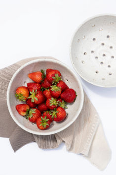 a white bowl filled with strawberries on top of a table next to a cloth