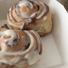 two cinnamon rolls in a white box with icing