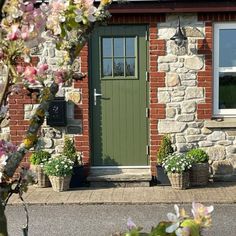 a green door and window in front of a brick building with flowers on the outside