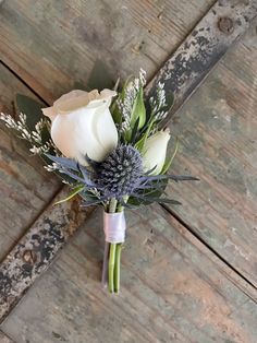 a boutonniere with white roses and greenery on an old wooden background