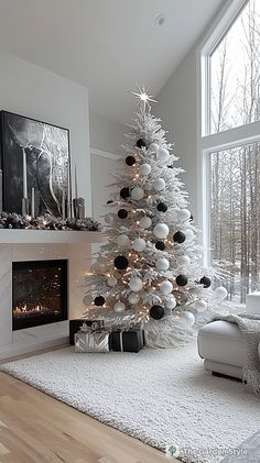 a white christmas tree with black and silver ornaments is in front of a large window