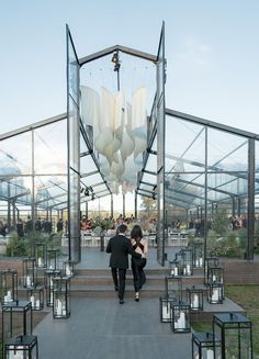 two people walking down a walkway in front of a glass structure with lanterns hanging from the ceiling