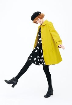 a woman in a yellow coat and black dress with stars on the skirt is walking