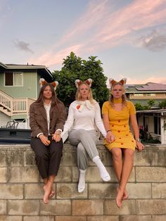 three women are sitting on a wall with their legs crossed and one is wearing cat ears