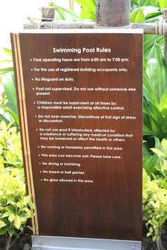 a sign describing the swimming pool rules in front of some trees and bushes with green leaves