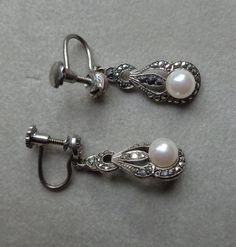 Small, elegant,  sterling silver, screw-back dangle earrings. Top part is patterned, in a semi-circular shape and ornamented with a single marcasite. Dangle is in an elongated, soft teardrop shape, with three semicircles and gentle curves shielding vertical, eye shaped cut-out center. Sparkling, bead set marcasite are placed through-out in a nice contrast to a rather large, creamy white faux pearl. Both earrings weight 5.01 grams and are well made with beaded metal edges and appealing pattern. Silver Pearl Drop Clip-on Earrings For Evening, Vintage White Gold Clip-on Earrings, Vintage Clip-on White Gold Earrings, Elegant Drop Earrings With Screw Back, Antique Silver Clip-on Earrings For Wedding, Ornate Silver Clip-on Earrings, Ornate Silver Clip-on Earrings For Formal Occasions, Silver Clip-on Pearl Earrings For Evening, Ornate Silver Pearl Earrings For Formal Occasions