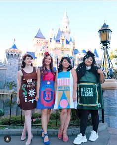 three girls dressed up in costumes standing next to each other near a castle at disneyland