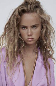 a woman with long blonde hair wearing a purple shirt and holding a brown leather necklace