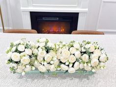 white flowers are arranged on a table in front of a fireplace