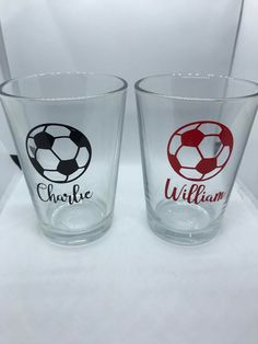 two personalized shot glasses sitting on top of a white table with red and black soccer balls