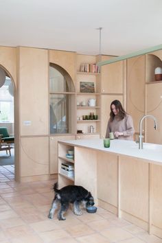 a woman standing in a kitchen next to a dog