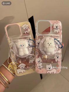 two cell phones are in the shape of animals and dogs on clear plastic cases, one is holding a keychain