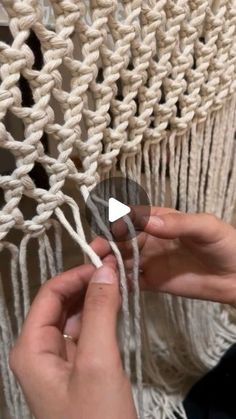 two hands are working on a macrame weaving project with white yarn and scissors