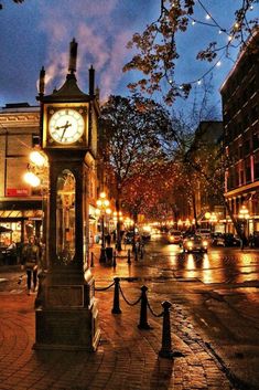 a clock tower sitting in the middle of a street at night time with people walking around