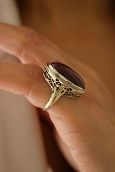 a woman's hand holding a gold ring with a large brown stone on it