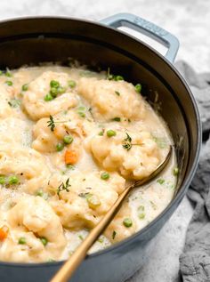 a pot filled with dumplings and peas on top of a table next to a wooden spoon