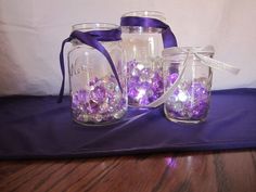 three glass jars with purple and white beads in them sitting on a blue table cloth