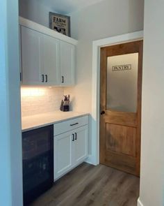 an empty kitchen with white cabinets and black appliances in the corner, next to a wooden door