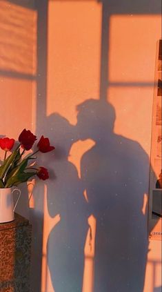 the shadow of a person standing next to a vase with flowers in it and a poster behind them