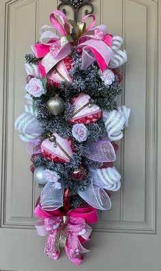 a wreath is hanging on the front door with pink and silver ribbons, ornaments, and bows