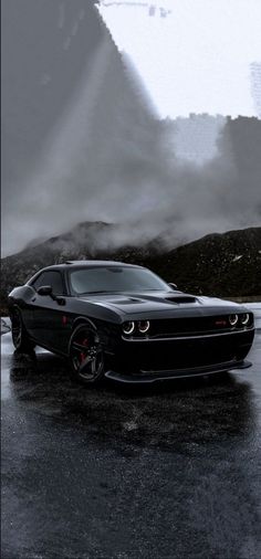 a black car parked on the side of a road in front of mountains and clouds